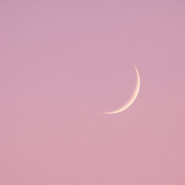 "Croissant de lune fin dans un ciel rosé poudré, symbole de transformation douce et d’introspection"